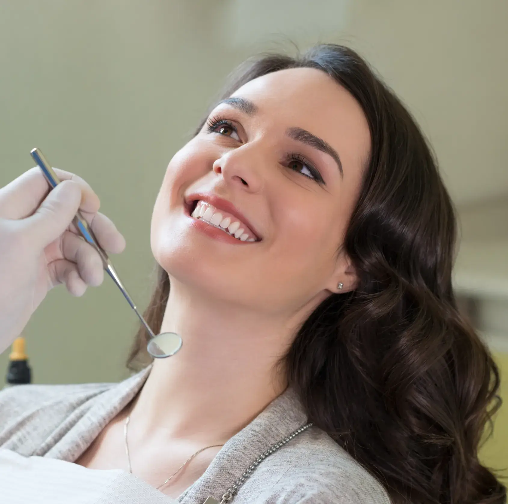 Smiling woman with dark hair having a dental checkup by a gloved hand with a dental mirror.