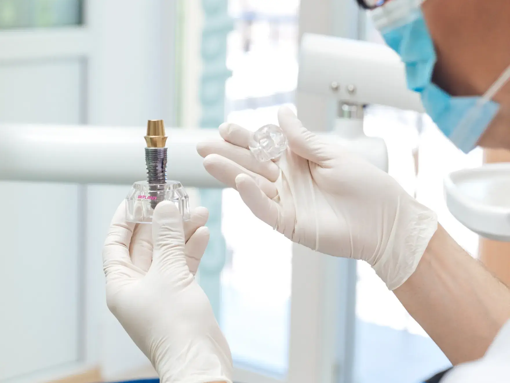 Dentist wearing gloves holding a dental implant model and a clear dental crown.
