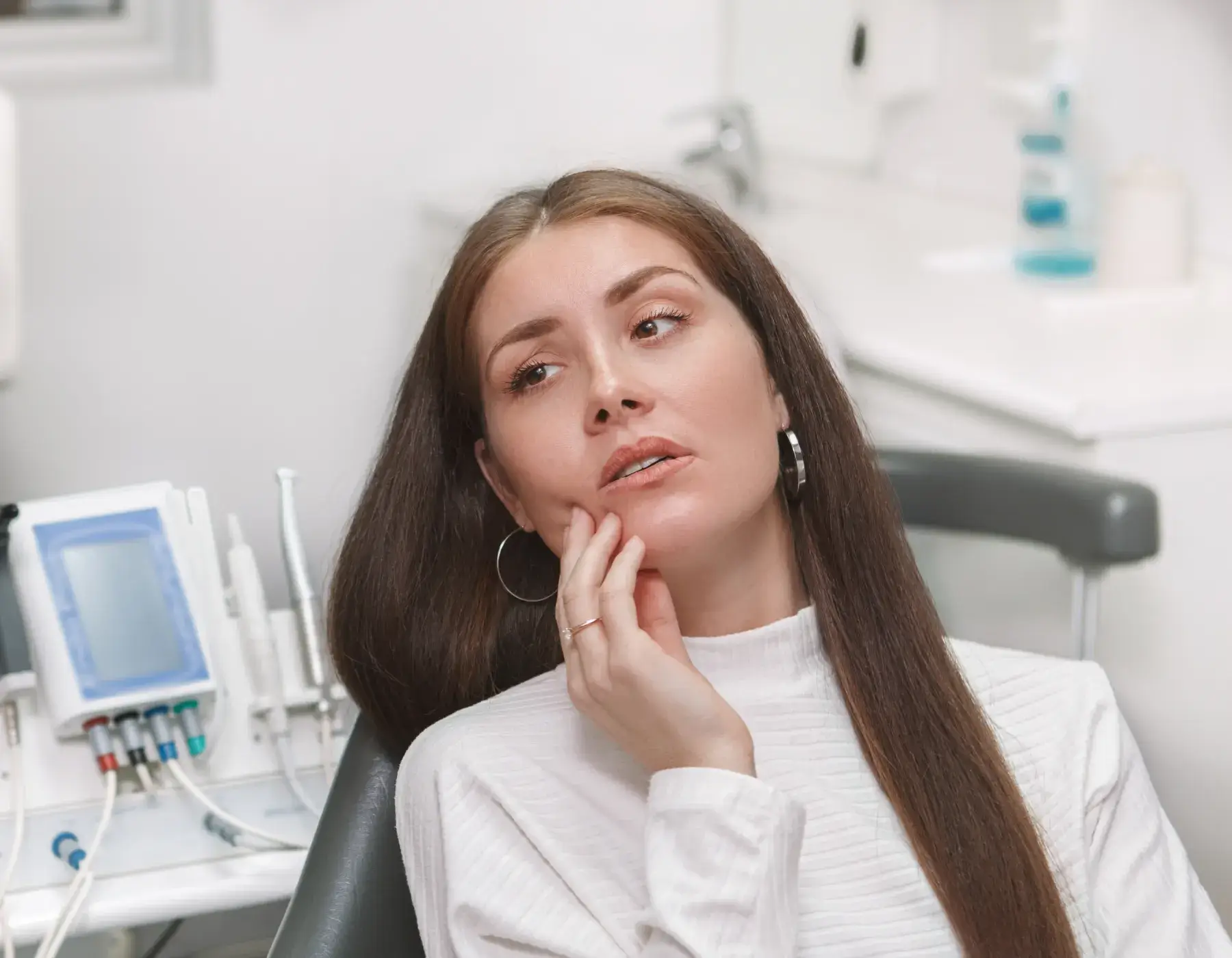 Woman sitting in dental chair holding her cheek showing tooth pain or discomfort.